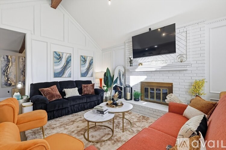 A living room with a black couch, orange chairs, and a fireplace.