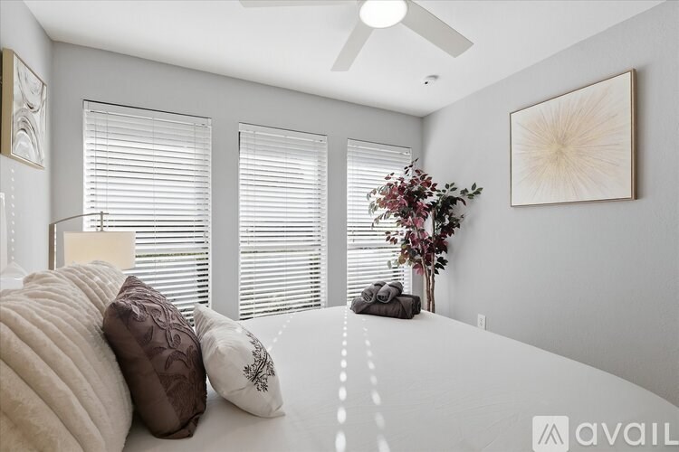 A room with a bed, pillows, a ceiling fan, and a plant.