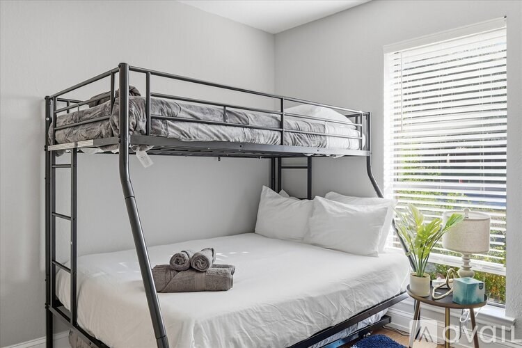 A white bed with a grey pillow and a grey blanket with a pair of glasses on top of it.