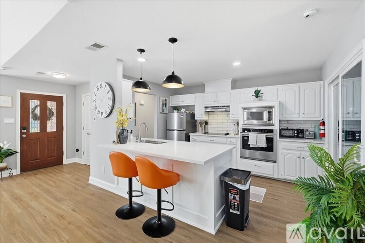 A kitchen with a white island and two orange barstools.