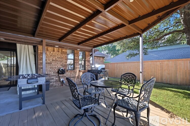 A patio with a table and chairs under a wooden roof.
