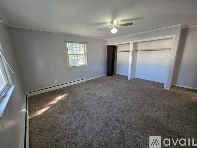 A room with a carpeted floor, a ceiling fan, and a window.
