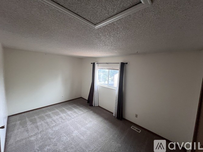 A room with a carpeted floor and a window with curtains.