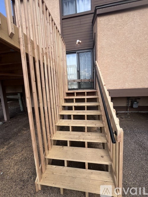 A wooden staircase with a black handrail is in front of a building.