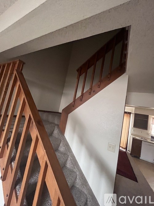 A staircase with wooden railings and a grey carpeted floor.