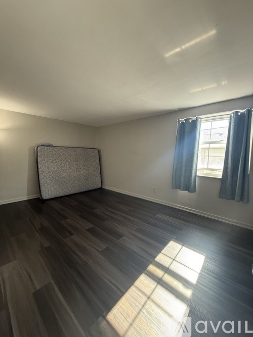 A room with a grey carpet, wooden floor and a window with blue curtains.