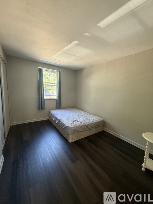 A bedroom with a bed, a window with curtains, and a small white table.