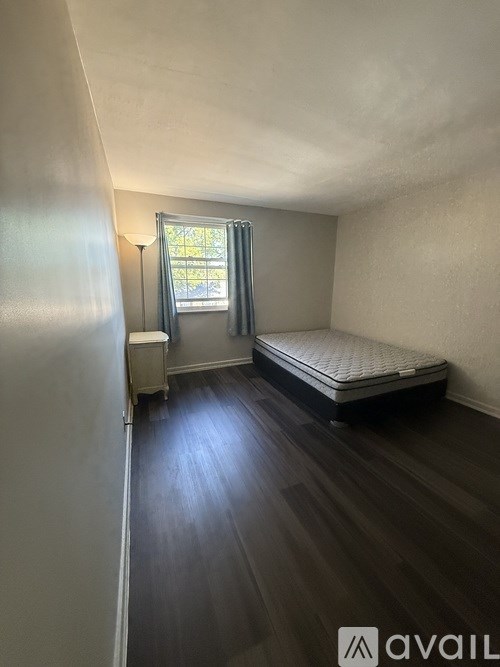 A bedroom with a bed, a window with curtains, and a wooden floor.