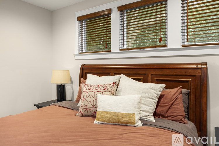 A bed with a brown comforter and pillows in front of a window with blinds.