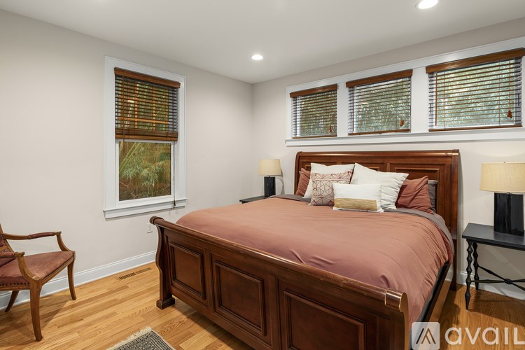A bedroom with a large bed, a chair, and a window with blinds.