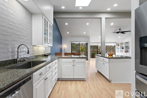 A modern kitchen with white cabinets and a wooden floor.