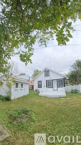 A small white house with a porch is surrounded by a white picket fence and green grass.
