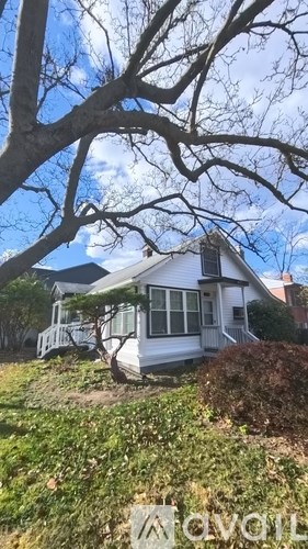 A small white house with a porch and a tree in the background.