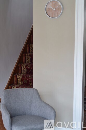 A grey chair is in front of a wall with a clock on it.