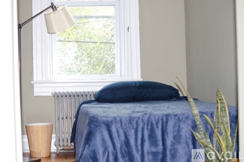 A blue bed with a white lamp and a window with a view of trees.