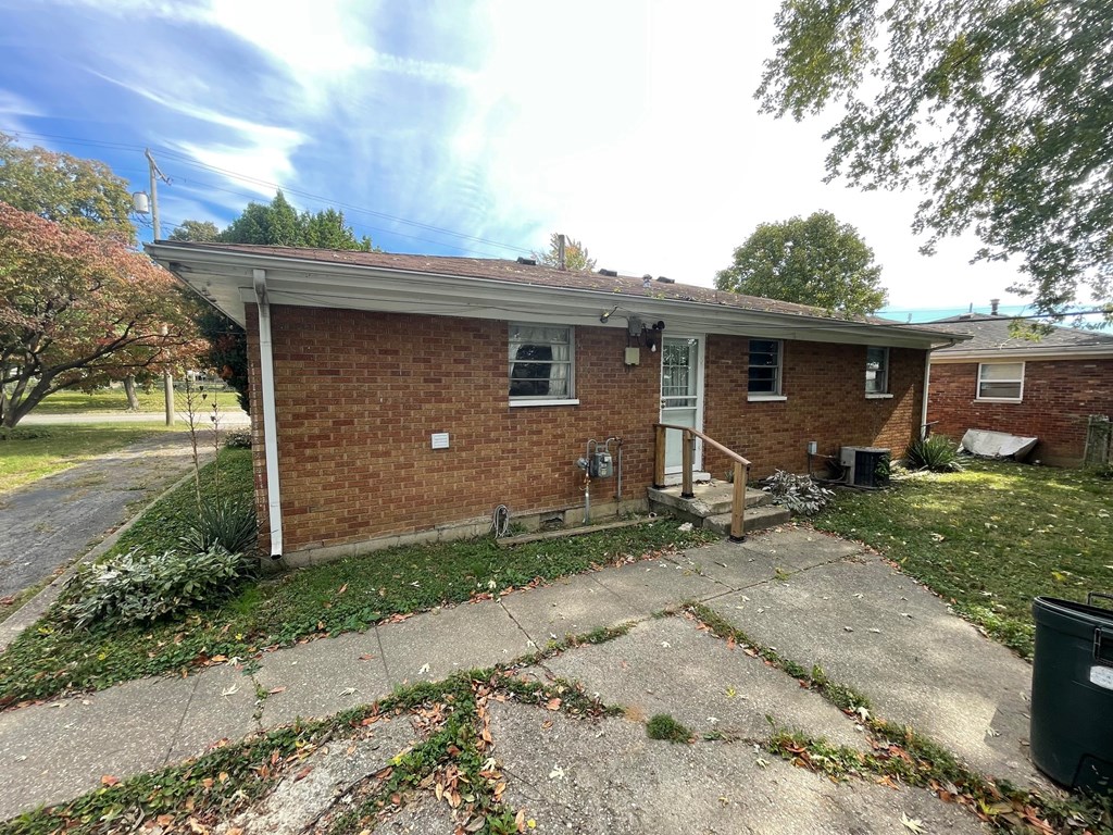 A small brick house with a porch and a tree in front.