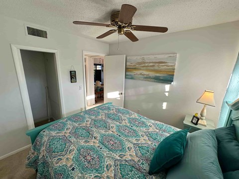 A bedroom with a bed covered in a patterned bedspread and a ceiling fan.