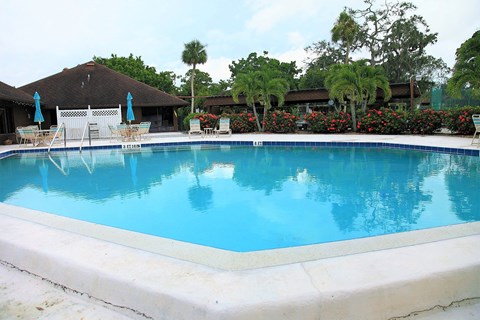 A large swimming pool with a white lounge chair and umbrella.