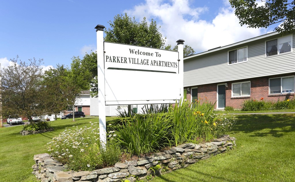 A sign that says "Welcome to Parker Village Apartments" stands in front of a building.