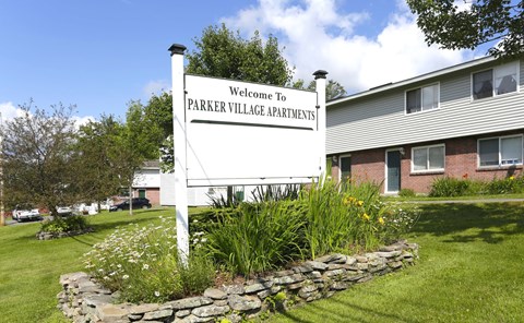 A sign that says "Welcome to Parker Village Apartments" stands in front of a building.