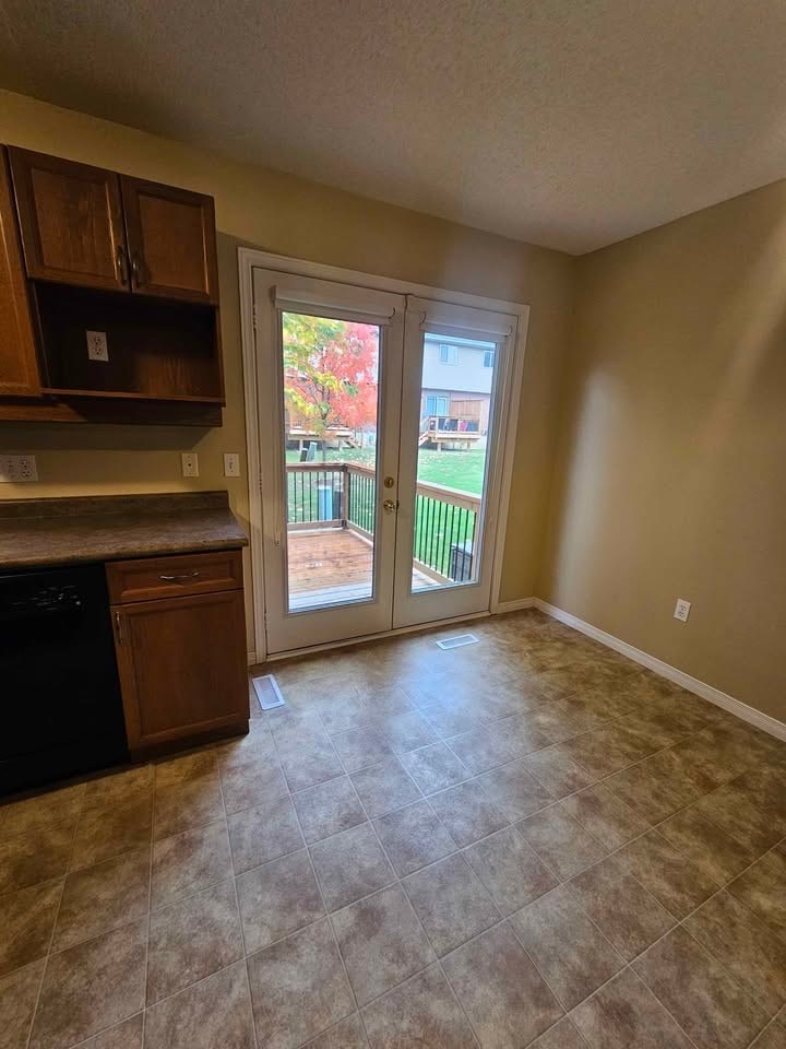 A kitchen with a black dishwasher and wooden cabinets.
