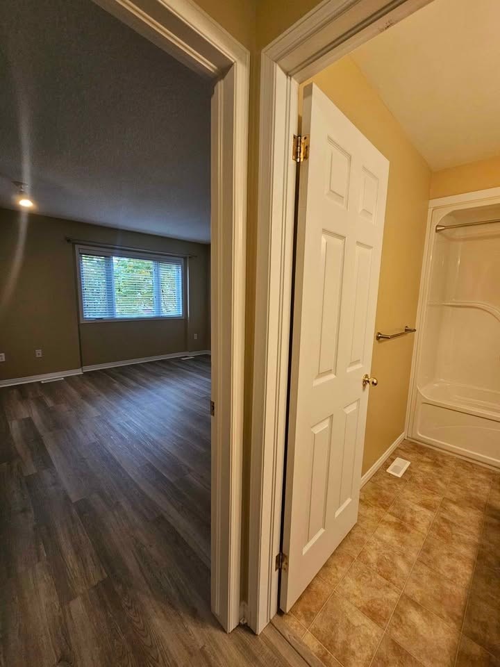 A white door is open to a room with wood flooring.