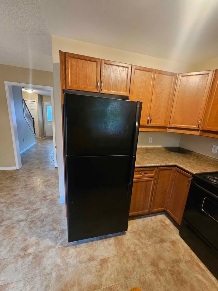 A black refrigerator stands in a kitchen with wooden cabinets.
