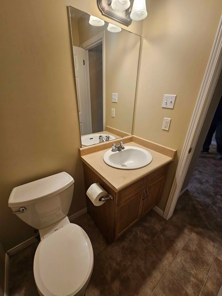A bathroom with a toilet, sink, and mirror.