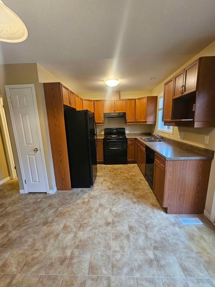 A kitchen with a black refrigerator and wooden cabinets.