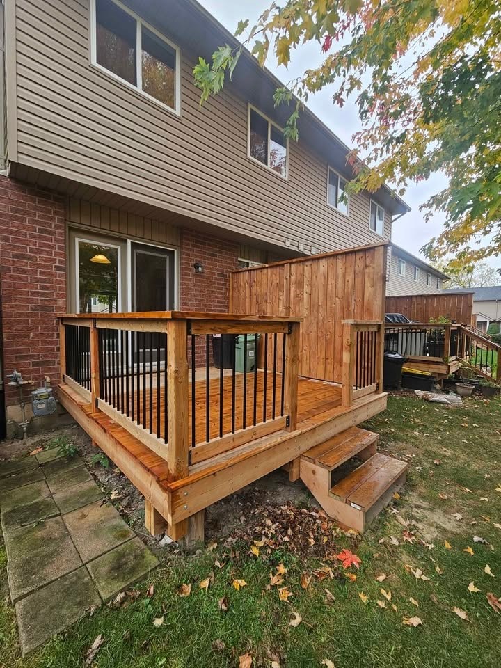A wooden deck with a railing and steps leading up to a house.