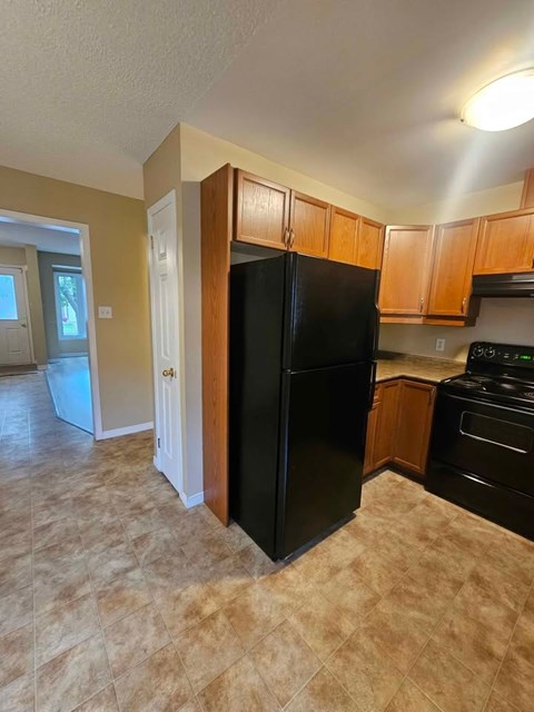 A black refrigerator in a kitchen with wooden cabinets.