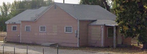 A small pink building with a grey roof and a fence in front of it.