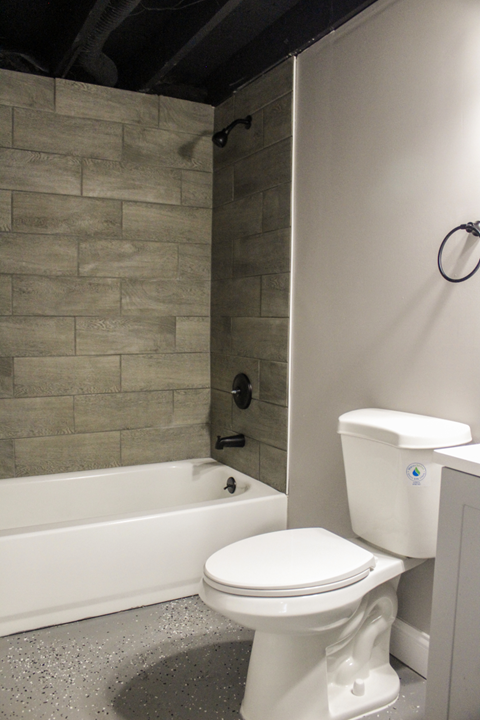 A white toilet in a bathroom with a grey tiled wall.