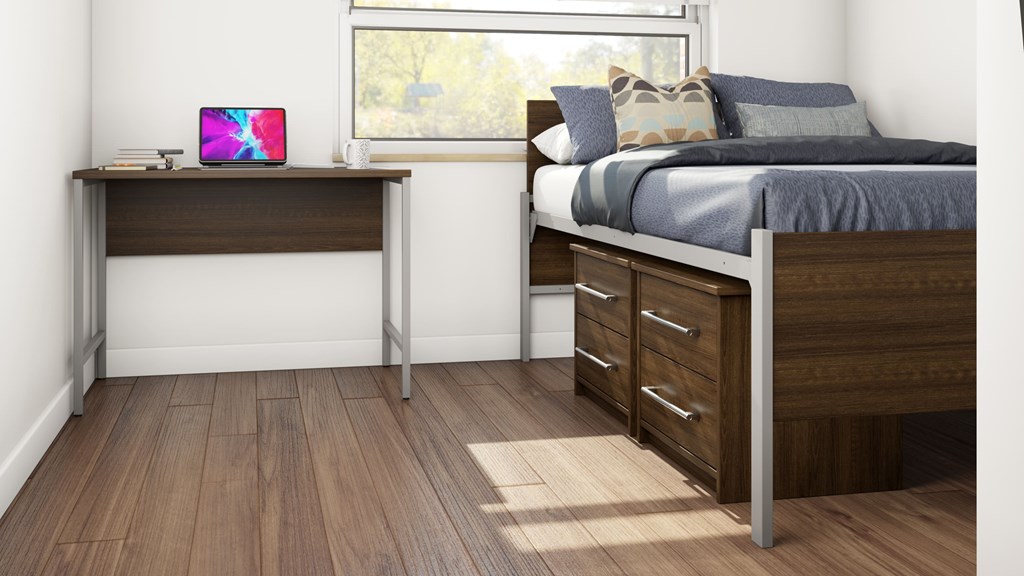 A laptop is on a desk in a bedroom with a bed and a window.