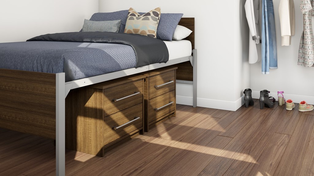 A bed with a grey blanket and pillows is in a room with wooden flooring and a wooden nightstand with drawers.