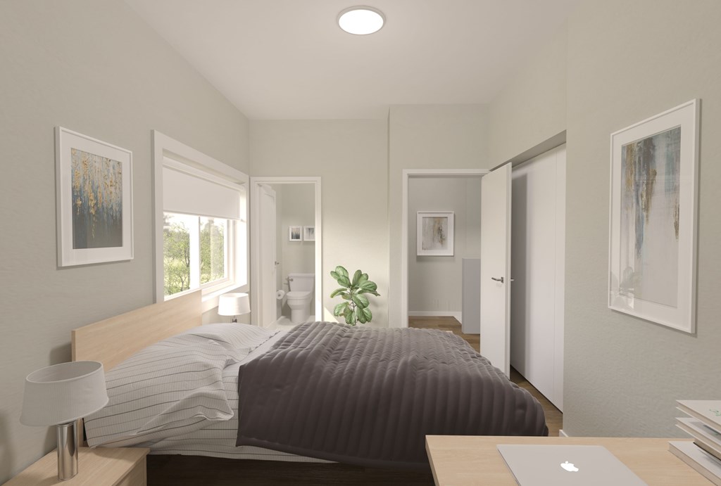 A bedroom with a bed, a laptop on the desk, and a plant on the windowsill.