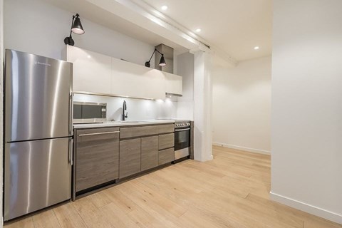 A modern kitchen with a stainless steel refrigerator and wooden flooring.