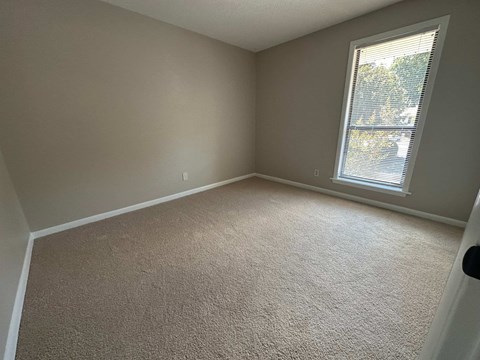 A room with a carpeted floor and a window with blinds.