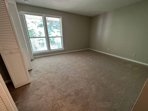 A room with a carpeted floor and a window with blinds.