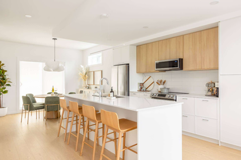 A modern kitchen with wooden chairs and white countertops.