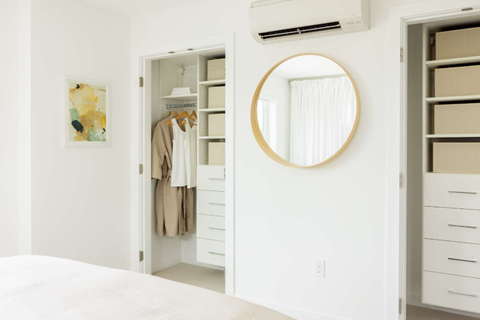 A white bedroom with a round mirror and a wardrobe.