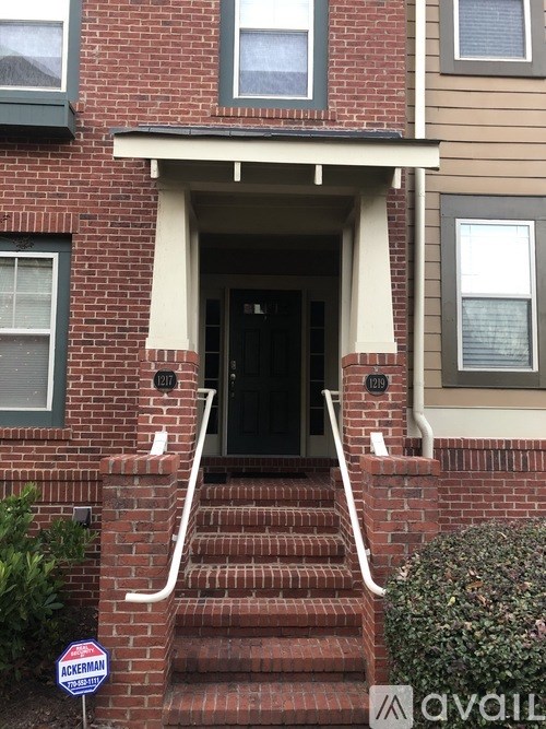 A red brick house with a black door and a sign that says "For Sale".