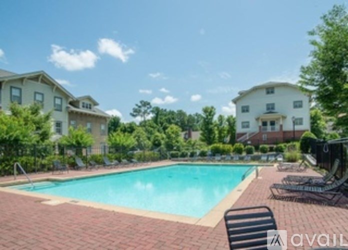A swimming pool surrounded by lounge chairs and trees with apartment buildings in the background.