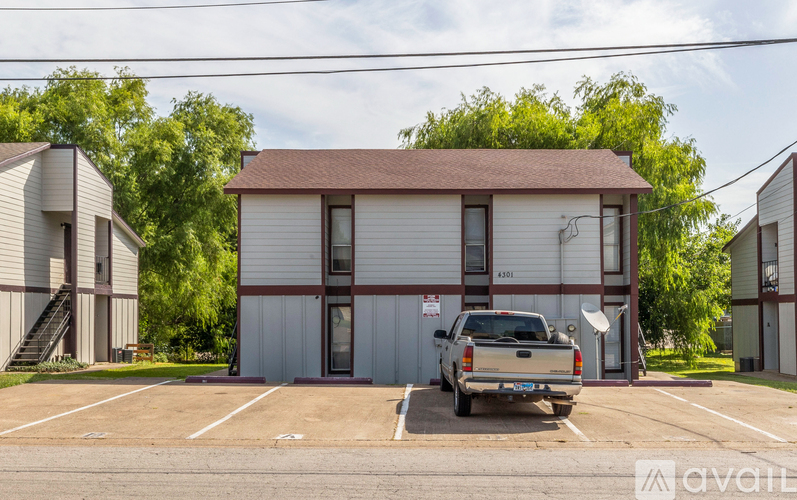 A silver pickup truck is parked in a parking lot in front of a two-story building with a brown roof.