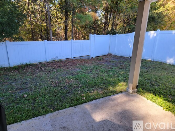 A white fence encloses a grassy area with a concrete walkway and a pillar.