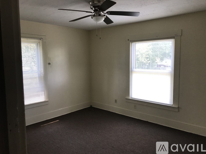 A room with a ceiling fan and two windows.