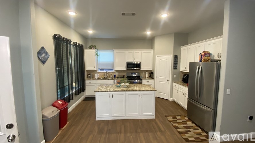 A kitchen with white cabinets and a central island with a marble top.