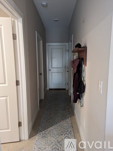 A hallway with a rug on the floor and a coat rack on the wall.