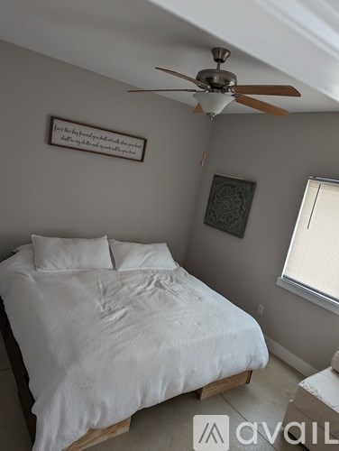 A bedroom with a bed, a ceiling fan, and a picture on the wall.