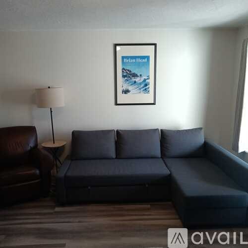 A living room with a grey couch, a brown leather chair, and a painting of a beach scene.